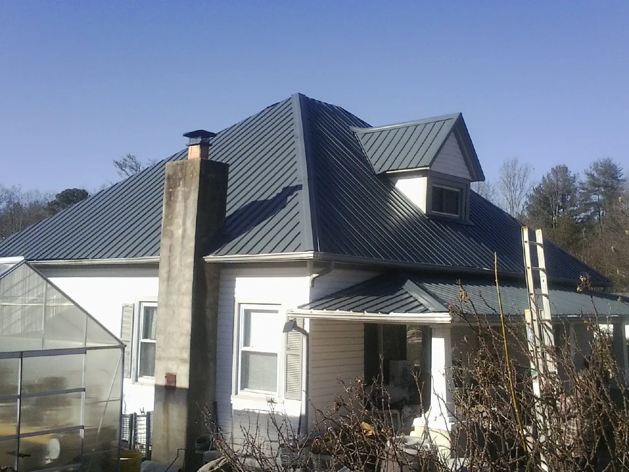 Dark blue standing seam metal roof on a white farmhouse with dormer — Slate & Tile Roof Repair by Roofing Brothers in Camdenton