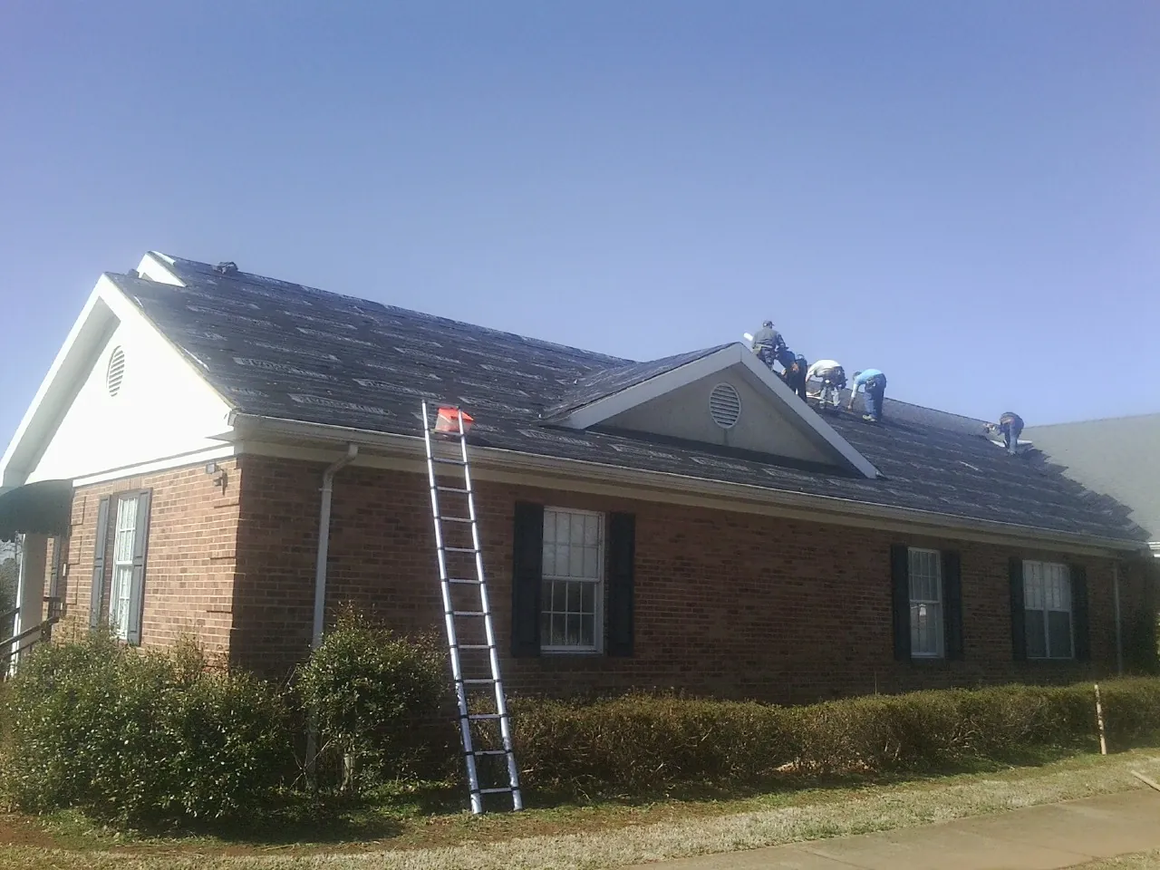 Crew tearing shingles off a brick ranch roof with a ladder set — Metal Roof Repair work by our crew in Camdenton