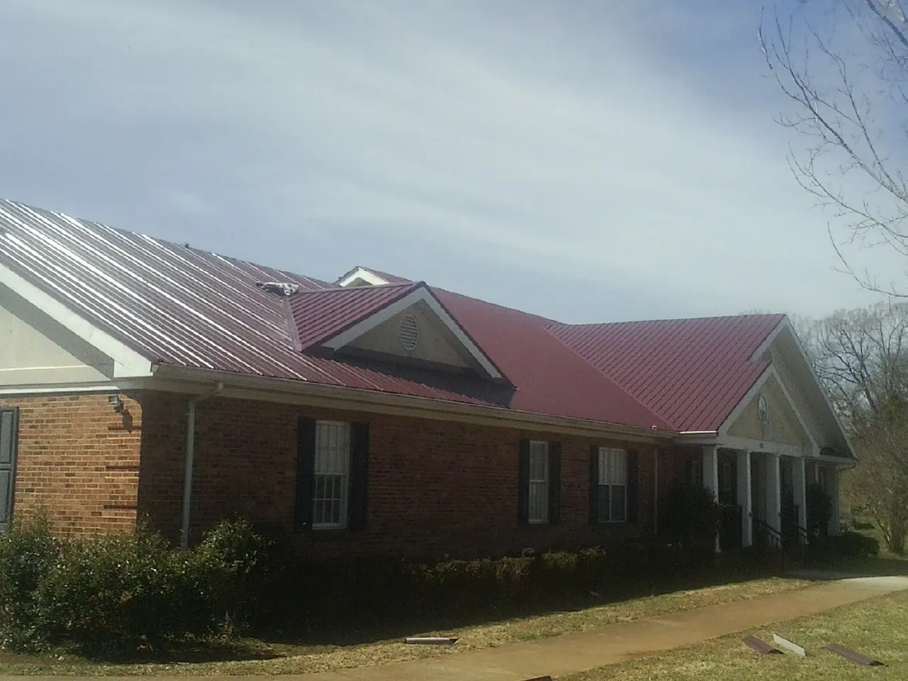 Red metal roof with gabled entries on a long brick building, from a Hail Damage Roof Repair job in Camdenton