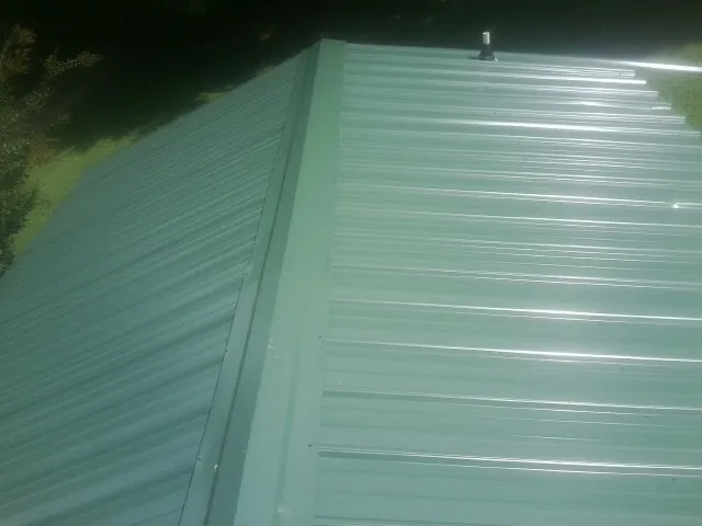 New green metal panels meeting at the ridge of a roof — Flat Roof Repair work by our crew in Camdenton