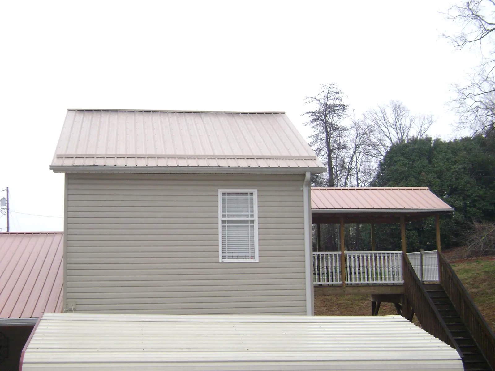 Tan metal roofs on a two story addition and attached porch, from a Roof Replacement job in Camdenton